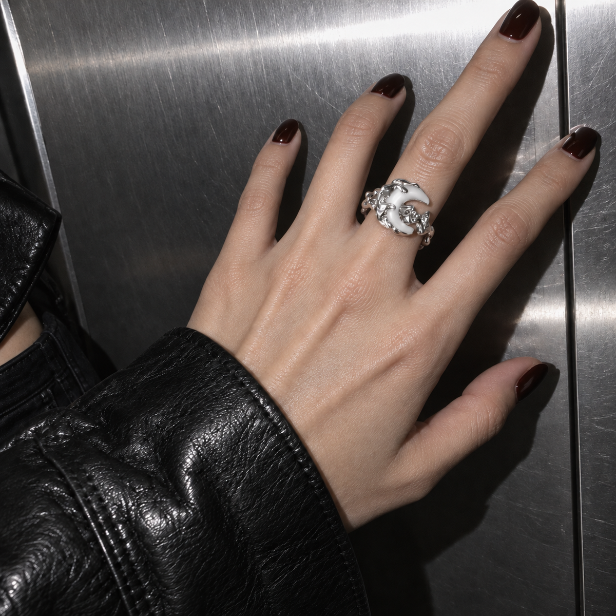Crescent moon ring worn on a hand beside a metal wall