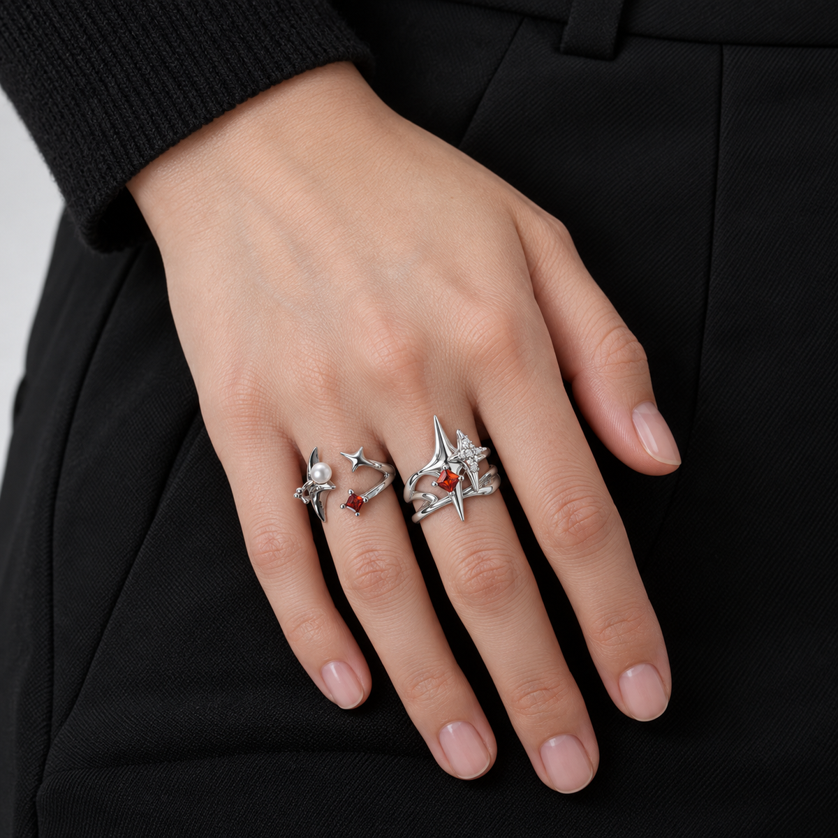 Close-up of two silver-tone red-stone celestial ring styles worn on a hand against black clothing