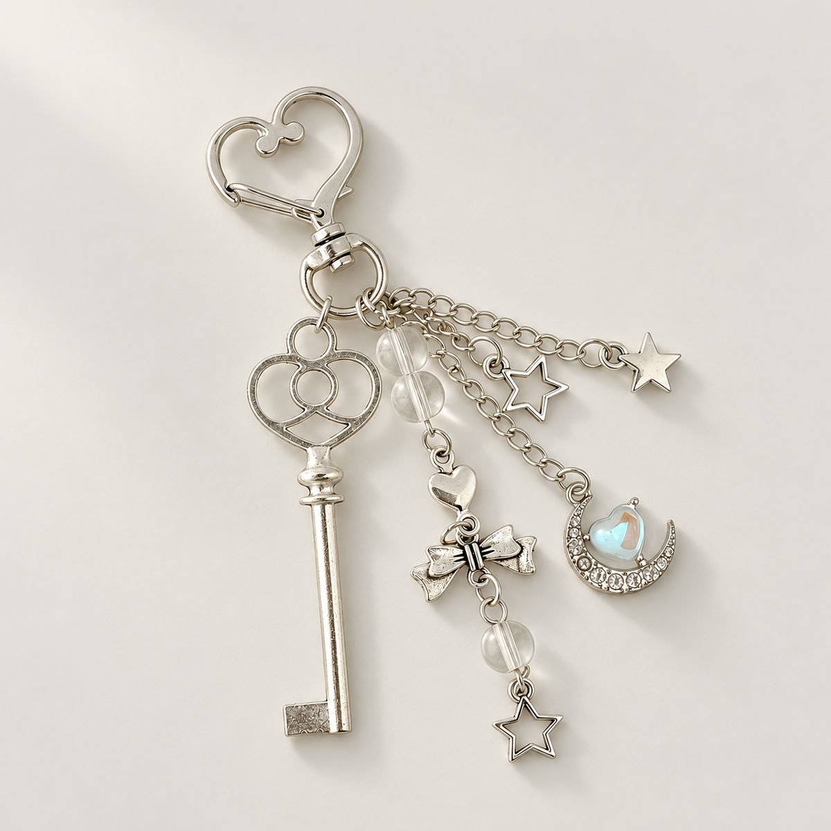 Silver key and moon charm keychain on warm off-white background