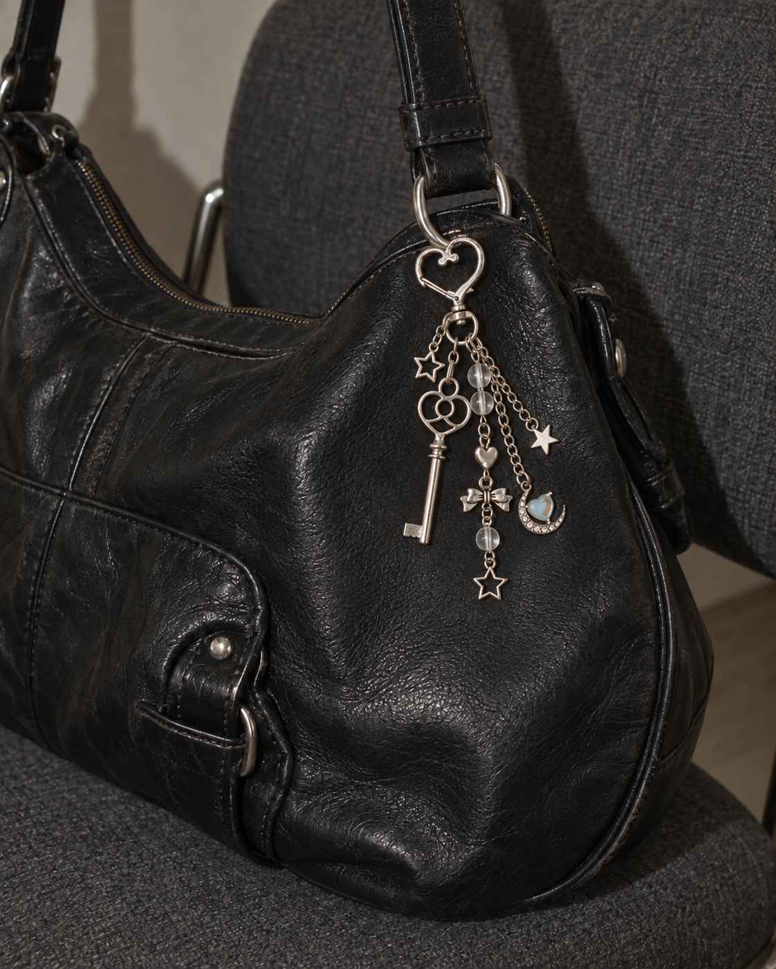 Silver key and moon charm keychain hanging from a black leather bag